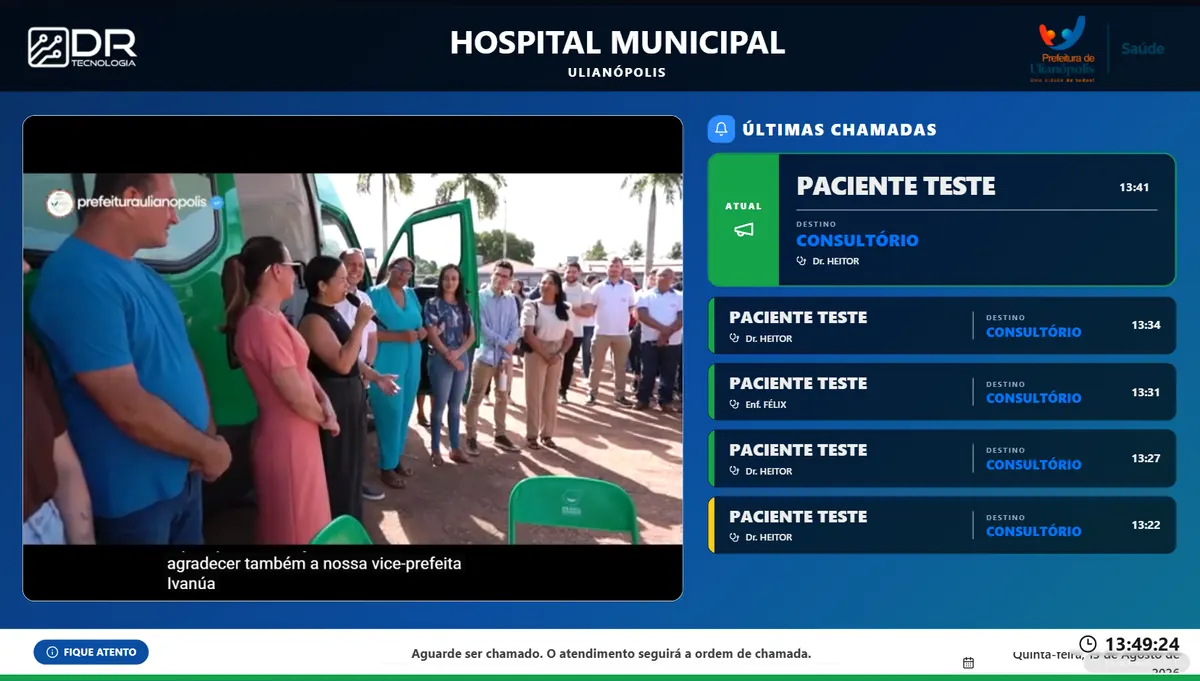 Painel Synk em uma unidade de saúde, com conteúdo multimídia à esquerda e fila de chamadas, destino e horário à direita.